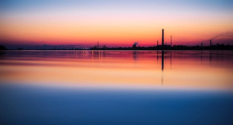 A stunning view of an industrial landscape with a vibrant sunset reflecting over calm waters.