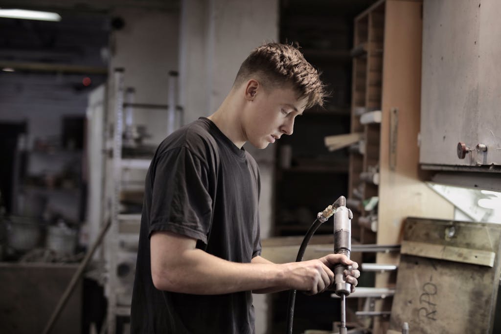 Side view of young male worker using pneumatic tool for handling detail in workshop